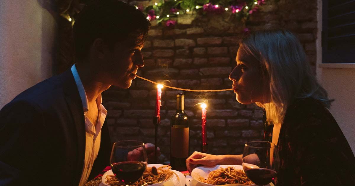 Couple sitting at candle-lit dinner sharing spaghetti.
